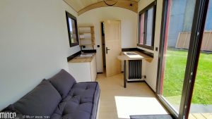 Intérieur d'une tiny house : cuisine et salon. Porte-fenêtre en bois aluminium Minco.